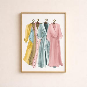 May include: An art print featuring four watercolor robes in a gold frame. The robes are in yellow, brown with blue polka dots, pink with black polka dots, and blue and white stripes. The last robe is a solid pink with a tie.