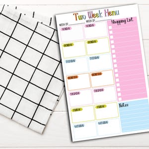May include: A colorful two-week menu planner with sections for each day of the week, a shopping list, and notes. The planner has a white background with a black and white checkered cloth on the left.