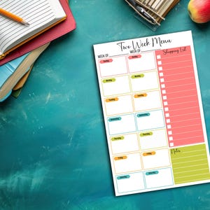 May include: A white Two-Week Menu planner with a shopping list section. The planner has boxes for each day of the week, with color-coded labels. A pencil, books, and an apple are in the background.