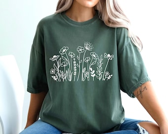 May include: A woman wearing a green oversized t-shirt with a white floral design. The shirt has a relaxed fit and is made of a soft, comfortable fabric.