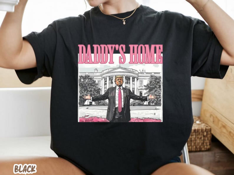 May include: Black t-shirt with the text "DADDY'S HOME" in pink. The graphic features a man in a suit with arms outstretched in front of the White House. The word "BLACK" is at the bottom of the shirt.