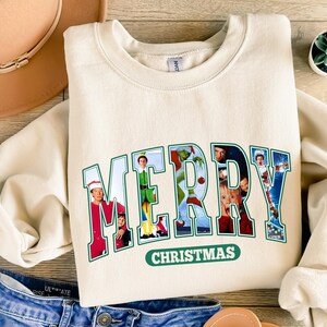 May include: A cream-colored sweatshirt with a green and white graphic print that says "MERRY CHRISTMAS" with images of characters from popular Christmas movies.