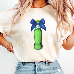 May include: A white t-shirt with a green Sprite bottle graphic. The bottle is tied with a blue bow.