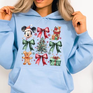 May include: Light blue hoodie with a Christmas-themed design featuring Mickey Mouse, a Christmas tree, bows, and gifts.