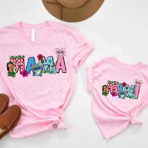 May include: Pink t-shirts with a "Mama" and "Mini" design featuring Stitch characters from Lilo & Stitch. The shirts have a floral and tropical theme.