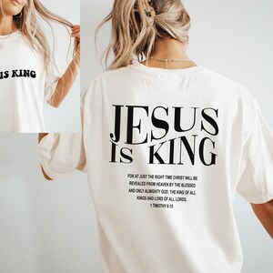 Puede incluir: Camiseta blanca con el texto "JESUS IS KING" impreso en negro en la parte delantera y trasera. La parte trasera tambi&eacute;n incluye un vers&iacute;culo b&iacute;blico de 1 Timoteo 6:15.