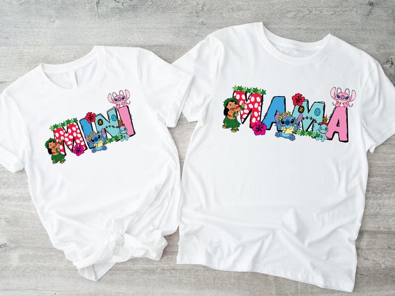 May include: Two white t-shirts with a blue and pink cartoon character design. The larger shirt says "MAMA" and the smaller shirt says "MINI".