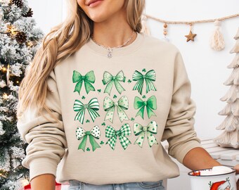 May include: A beige sweatshirt with a green shamrock and bow pattern. The bows are in various shades of green and white.