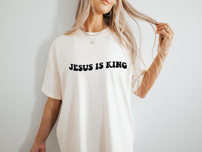 Puede incluir: Una camiseta blanca con el texto "JESUS IS KING" impreso en negro.