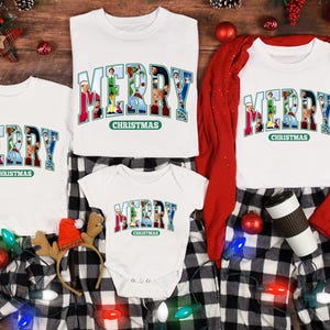 May include: A set of four white t-shirts with the words "Merry Christmas" printed on them. The word "Merry" is made up of images of Christmas characters. The shirts are arranged on a black and white checkered fabric with Christmas lights and ornaments.