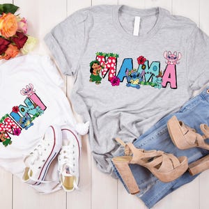 May include: Two white t-shirts with a colorful graphic print of the word "MAMA" and "MINI" with Stitch characters. The shirts are on a white wooden surface with a bouquet of red roses and a pair of white sneakers.