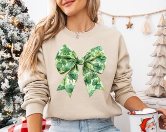May include: A beige sweatshirt with a green shamrock bow design. The bow is made of green shamrocks and has a watercolor effect.
