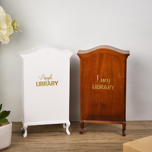 May include: Two miniature wooden bookcases, one white and one brown, with the words "Angel Library" and "Lucy Library" written on the front.