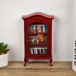 May include: A miniature red wooden bookcase with glass doors and shelves filled with books. A bouquet of orange flowers is placed on the top shelf.