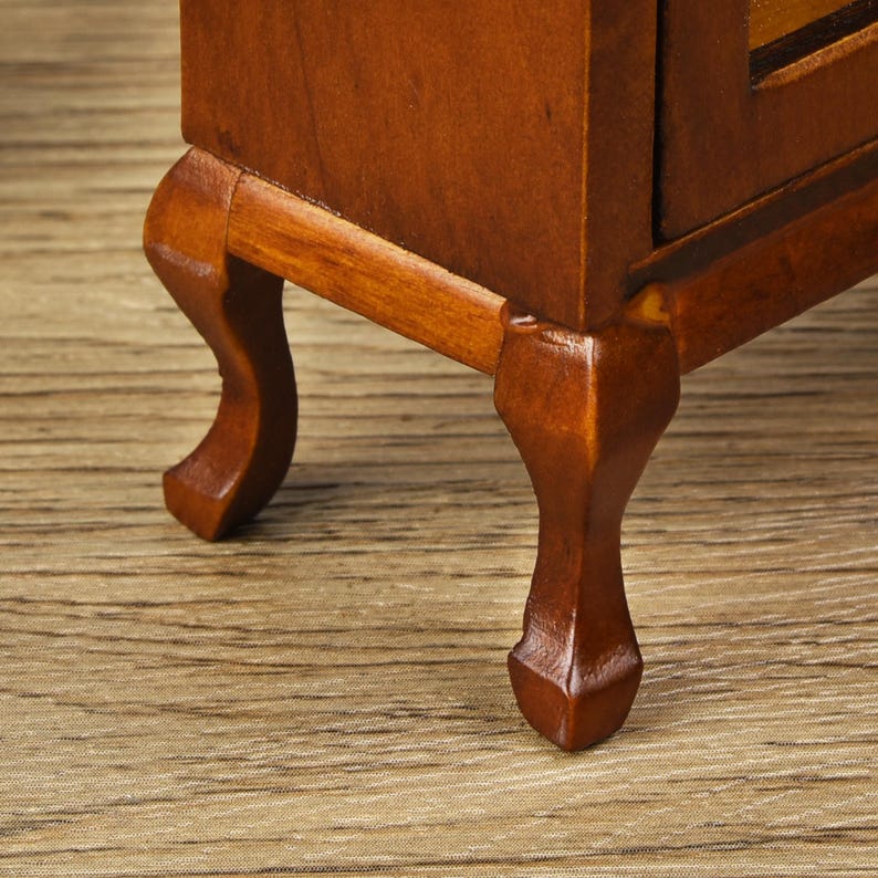 May include: Close-up of the bottom of a wooden cabinet with four legs. The legs are carved in a cabriole style and have a dark brown finish.