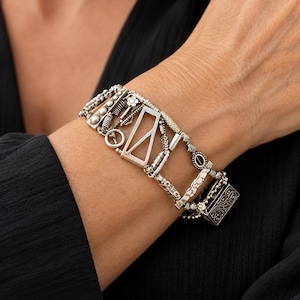 May include: A silver-toned charm bracelet featuring an assortment of geometric and textured links, including a rectangular frame, a small flower, coiled wire segments, and a rectangular clasp with an intricate engraved floral pattern.