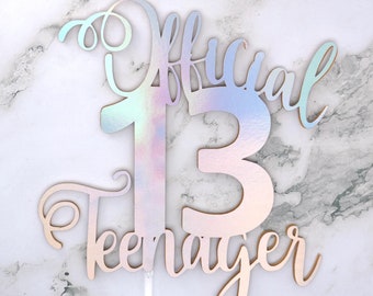Puede incluir: Un adorno para pastel con acabado de purpurina iridiscente, que presenta las palabras "Official Teenager" y el número "13".