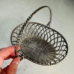 May include: A silver wire basket with a handle. The basket is oval shaped and has a woven design.