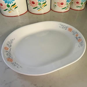 May include: White oval serving platter with a floral design in shades of pink, blue, and gray. The design features small flowers and leaves.