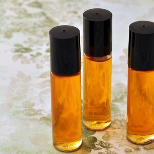 Puede incluir: Cuatro botellas roll-on de vidrio transparente con tapas negras, llenas de un l&iacute;quido de color dorado. Las botellas est&aacute;n dispuestas en fila sobre una superficie con estampado floral. La imagen est&aacute; bien iluminada, resaltando la transparencia del vidrio y el color del l&iacute;quido.