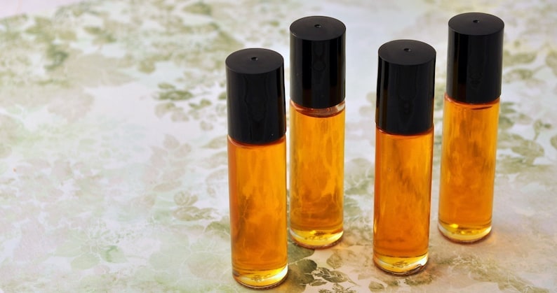 Puede incluir: Cuatro botellas roll-on de vidrio transparente con tapas negras, llenas de un l&iacute;quido de color dorado. Las botellas est&aacute;n dispuestas en fila sobre una superficie con estampado floral. La imagen est&aacute; bien iluminada, resaltando la transparencia del vidrio y el color del l&iacute;quido.
