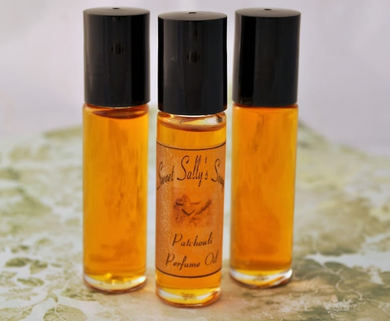 Puede incluir: Tres frascos de perfume roll-on de vidrio transparente con tapas negras. Los frascos contienen un l&iacute;quido dorado. Un frasco tiene una etiqueta que dice "Sweet Sally's Soap Patchouli Perfume Oil."