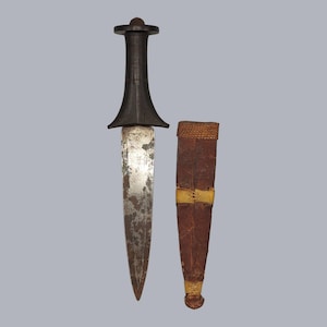 May include: A black-handled dagger with a silver blade and a brown leather sheath. The dagger has a decorative design on the handle.