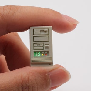 May include: A miniature white computer tower with a green digital display showing "3:21" and red and yellow lights. The tower has a series of slots and buttons.
