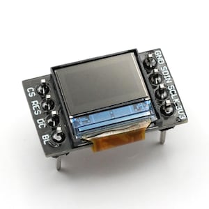 May include: A small, rectangular electronic component with a screen. The component is black with a rectangular display and several pins. Text on the component includes "CS", "RES", "DC", "BL", "GND", "SDIN", "SCLK", and "303".