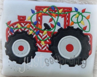 Puede incluir: Tractor de juguete rojo con ruedas negras y una guirnalda verde de luces navideñas envuelta alrededor. El tractor tiene un patrón de chevron rojo y blanco.