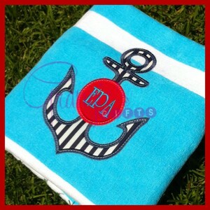 Op de afbeelding: Een blauw-wit gestreepte anker met een rode cirkel met het monogram "EPA" op een turquoise en wit gestreepte strandhanddoek.