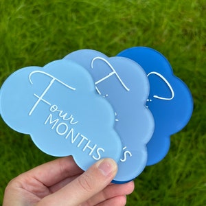 May include: Three blue cloud-shaped acrylic milestone cards with white text. The top card says "Four Months".