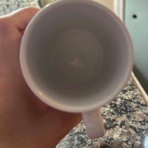 May include: A white ceramic mug viewed from directly above, showing the circular opening and the interior base. The mug features a smooth, glossy white finish on both the interior and exterior surfaces, with a single handle extending from the side.
