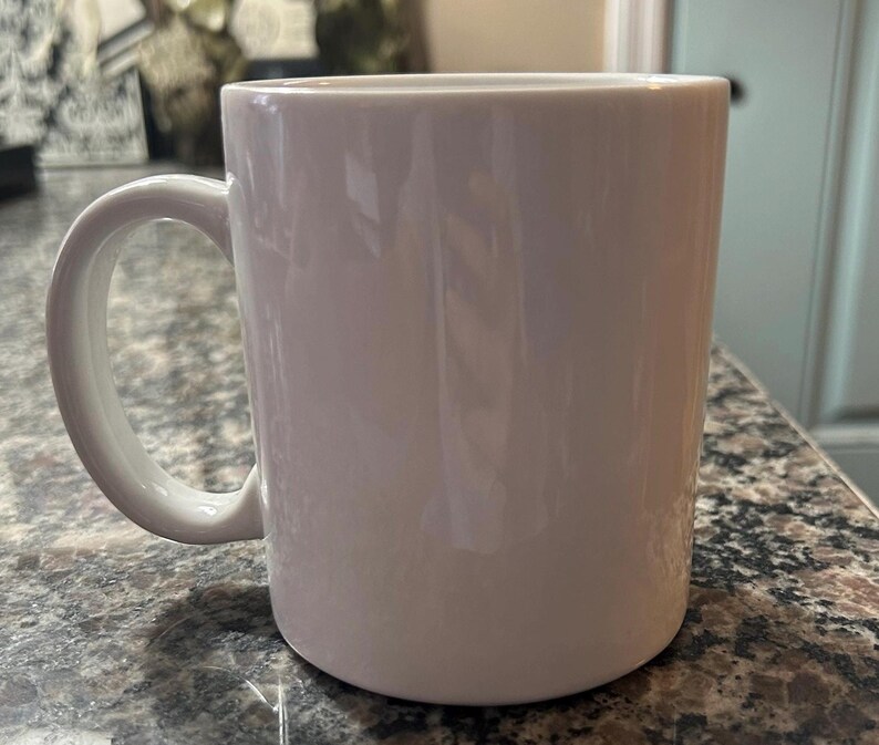 May include: A plain white ceramic mug with a smooth, glossy finish and a curved handle on the left side. The mug features a cylindrical body with a flat base and a wide, open top, presenting a clean, minimalist design suitable for hot beverages.