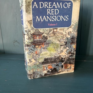 Könnte beinhalten: Ein gebundenes Buch mit dem Titel A Dream of Red Mansions Volume I. Das Cover zeigt eine detaillierte Tusche- und Aquarellillustration traditioneller ostasiatischer Architektur, Pagoden, Brücken und Figuren in einer Gartenlandschaft.