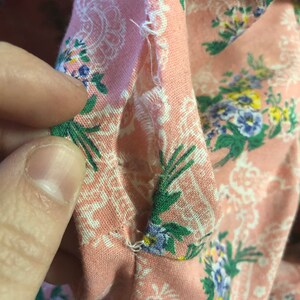 May include: Close-up of a section of pink floral fabric with a white paisley design. The fabric has a tear in the seam, revealing the raw edges and stitching. The fabric is decorated with small blue, green, and yellow flowers.