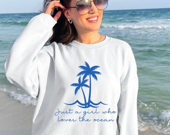 May include: White sweatshirt with a blue palm tree graphic and the text "Just a girl who loves the ocean".