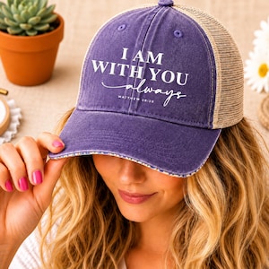 May include: A purple and tan trucker hat with the text "I AM WITH YOU always" in white script. The hat has a curved brim and a mesh back. The hat is a casual accessory.
