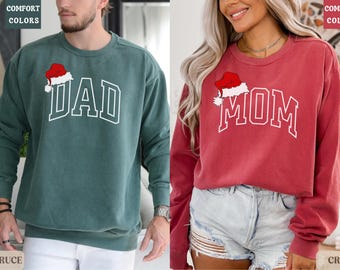 May include: Two Christmas themed sweatshirts, one green with "DAD" and a Santa hat, the other red with "MOM" and a Santa hat.
