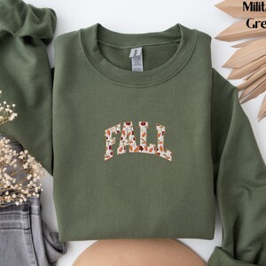 May include: A green sweatshirt with the word "FALL" printed on the front in a white font with a brown and orange floral pattern.