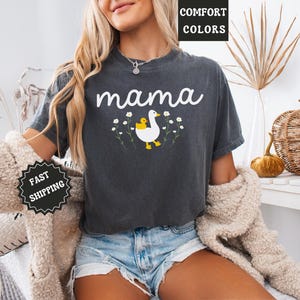 May include: A dark gray t-shirt with the word "mama" printed in white. A white duck with a yellow chick is printed on the shirt with a floral design around it.
