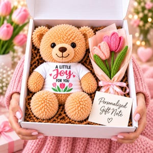 May include: A tan crochet teddy bear wearing a white t-shirt with the text A LITTLE JOY FOR YOU and pink tulip graphics, accompanied by a small bouquet of three crocheted pink tulips and a card labeled Personalized Gift Note with a heart symbol.