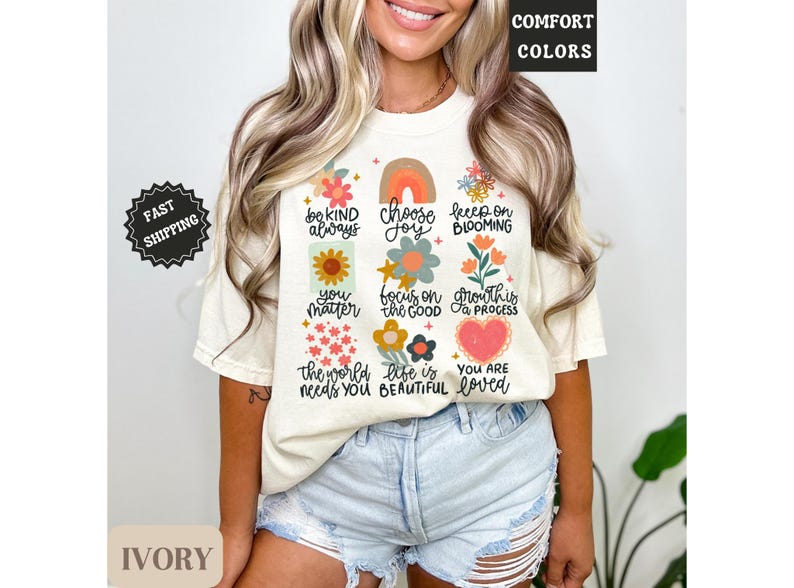 Pu&ograve; includere: Una maglietta color crema con un design floreale e affermazioni positive. Il testo sulla maglietta recita "Sii gentile sempre", "Scegli la gioia", "Continua a fiorire", "Tu conti", "Concentrati sul bene", "La crescita &egrave; un processo", "Il mondo ha bisogno di te", "La vita &egrave; bella", e "Sei amato".