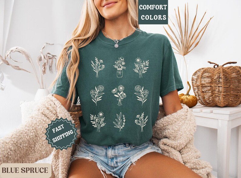 May include: A teal green t-shirt with a graphic of nine different floral arrangements in white. The text "COMFORT COLORS" is printed on the top left corner of the shirt.