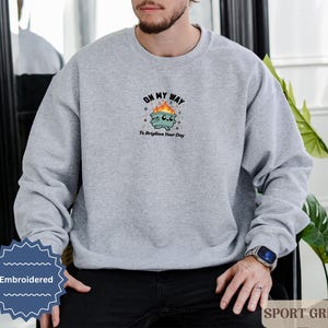 Pu&ograve; includere: Una felpa grigio chiaro con la scritta ricamata "OH MY WAY To Brighten Your Day" sopra un bidone della spazzatura dei cartoni animati con fiamme. La felpa &egrave; etichettata "SPORT GREY" ed &egrave; uno stile casual.