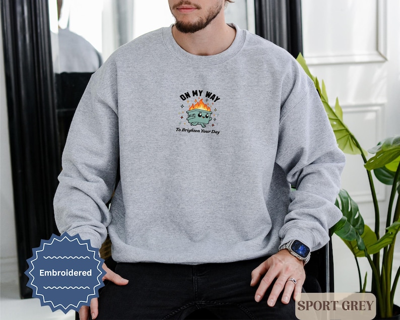 Pu&ograve; includere: Una felpa grigio chiaro con la scritta ricamata "OH MY WAY To Brighten Your Day" sopra un bidone della spazzatura dei cartoni animati con fiamme. La felpa &egrave; etichettata "SPORT GREY" ed &egrave; uno stile casual.
