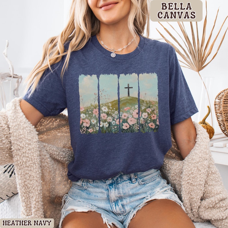 May include: Heather navy t-shirt with a floral and cross graphic. The graphic features a cross on a hill with flowers. The shirt is a Bella Canvas brand.