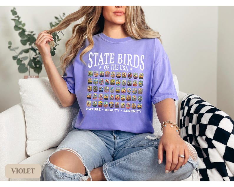May include: A woman wearing a purple t-shirt with the text "State Birds of the USA" and a graphic of birds. The shirt also has the text "Nature - Beauty - Serenity".