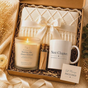 Peut inclure: Un coffret cadeau contenant une couverture en tricot crème nouée d'un ruban de satin, une bougie parfumée étiquetée 'leaving the chaos behind', un flacon d'allumettes, un mug blanc avec le texte 'Next Chapter' et une carte 'Gift Message INCLUDED'.