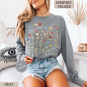 May include: Gray long-sleeve shirt with a floral design. The shirt features a watercolor-style illustration of colorful flowers in red, yellow, and blue. The words "Comfort Colors" and "Gray" are visible.